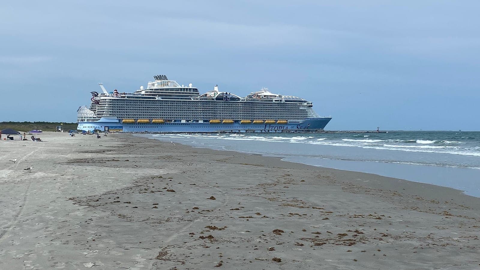 A large cruise ship leaving Port Canaveral past the beach