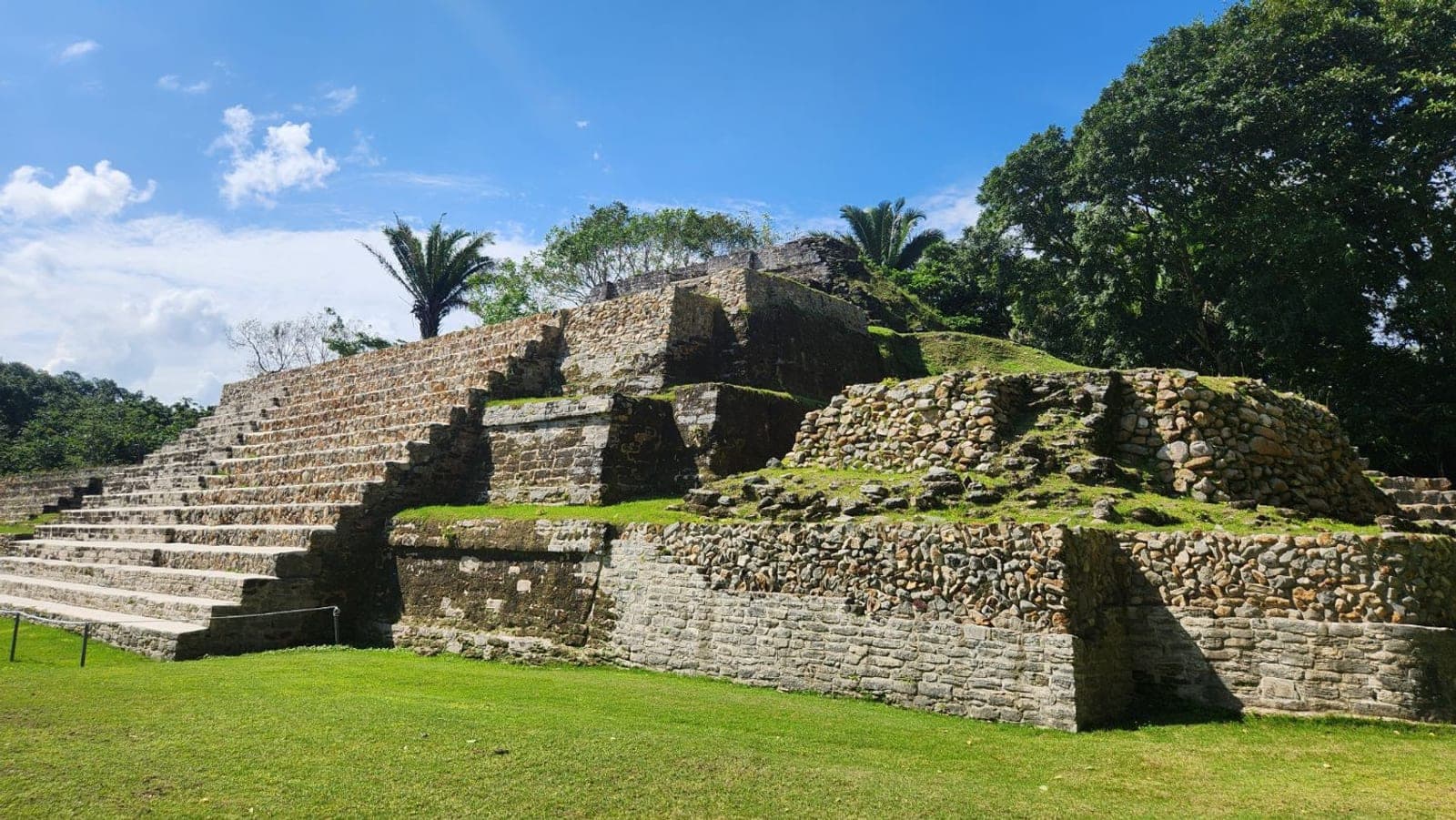 A grass-covered stepped Mayan temple pyramid at Altun Ha near Belize City, under a blue sky