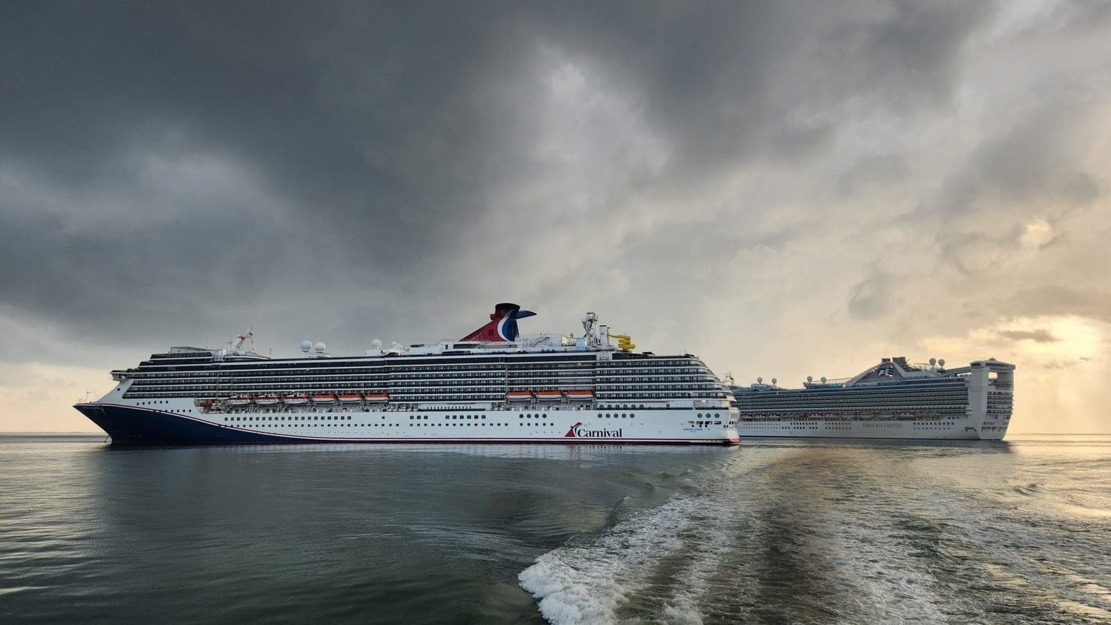 A Carnival ship and a Princess cruise ship anchored together off Belize City under a dramatic stormy sky