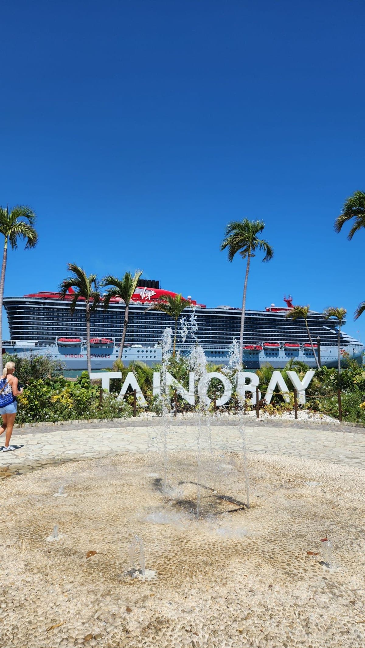 The Taino Bay cruise terminal sign and fountain in Puerto Plata with a Virgin Voyages ship docked behind