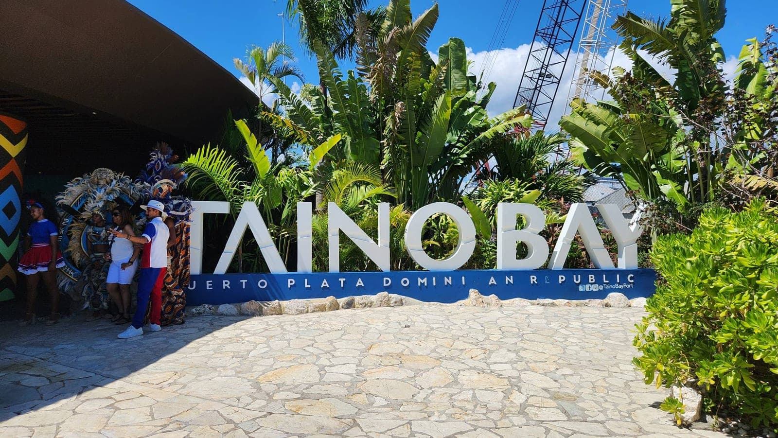 The 'Taino Bay, Puerto Plata Dominican Republic' entrance sign with performers in traditional costume