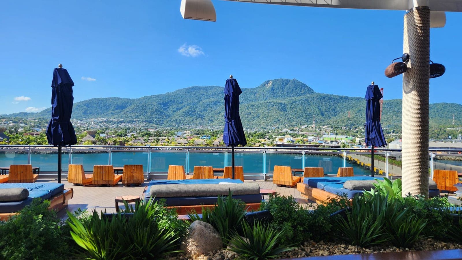 Daybeds and umbrellas on Valiant Lady's deck overlooking a mountainous port town
