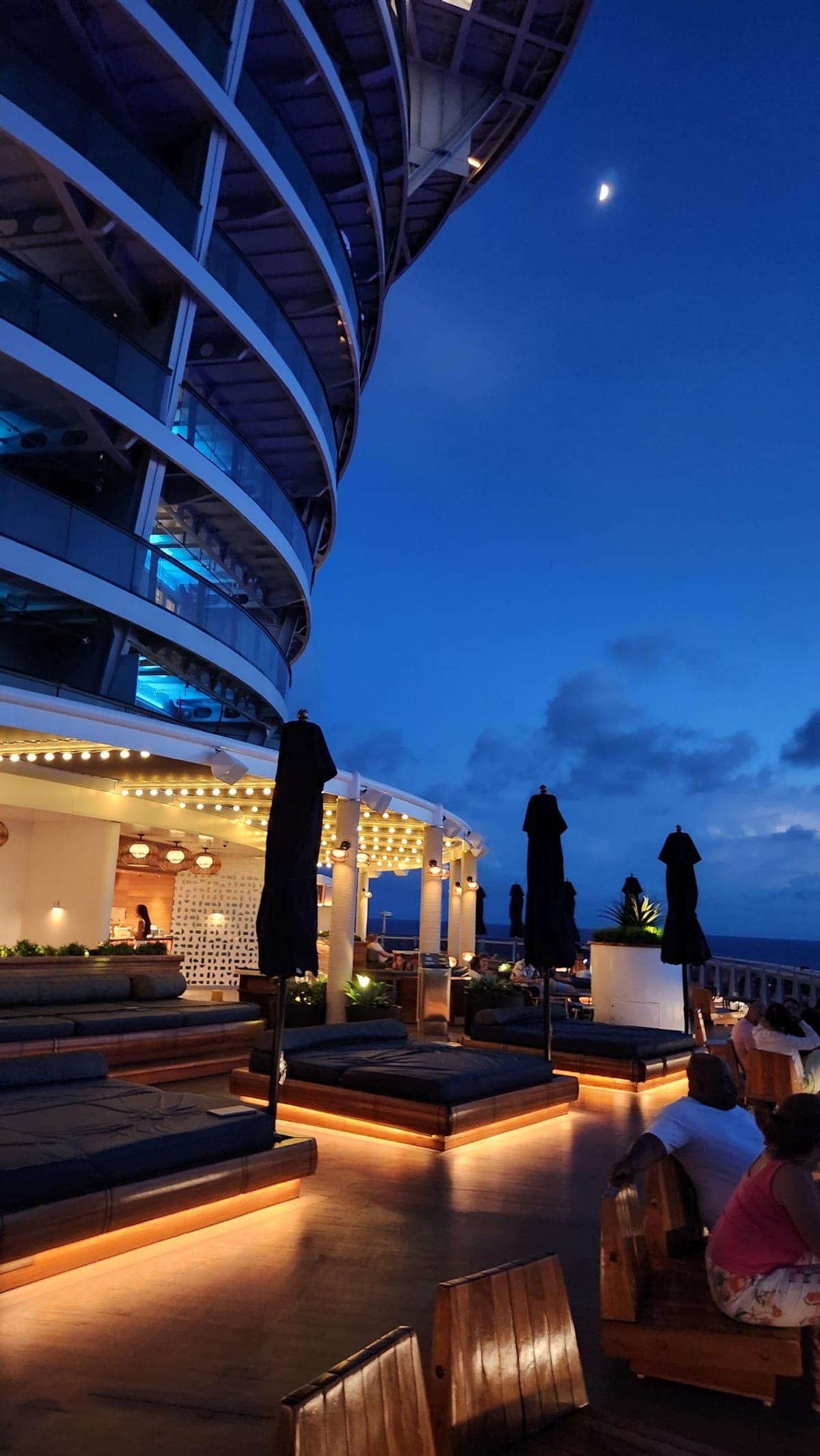Valiant Lady's rooftop deck at night with lit daybeds, string lights, and a crescent moon overhead
