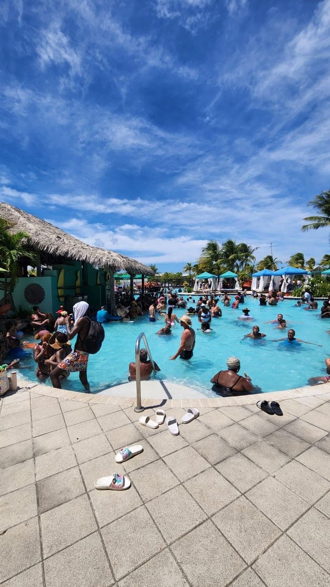 Busy swimming pool at Grand Turk Cruise Center with palm trees and thatched-roof facilities