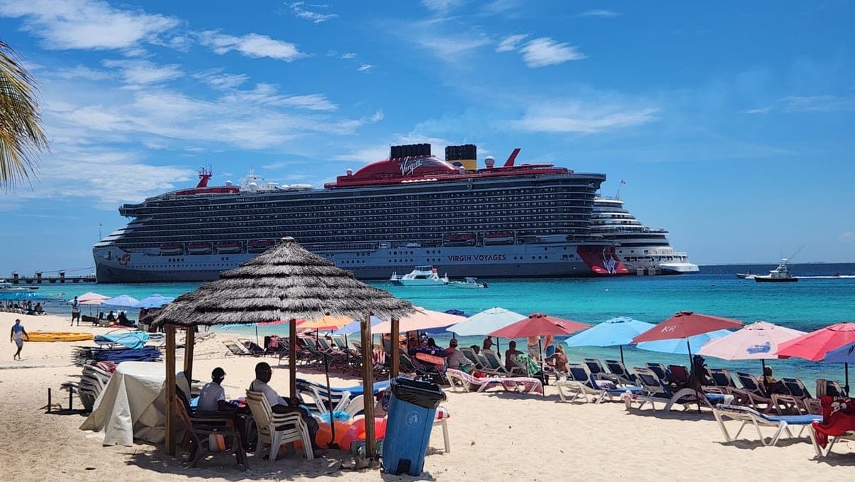Virgin Voyages cruise ship anchored beyond a sandy Grand Turk beach lined with colorful umbrellas