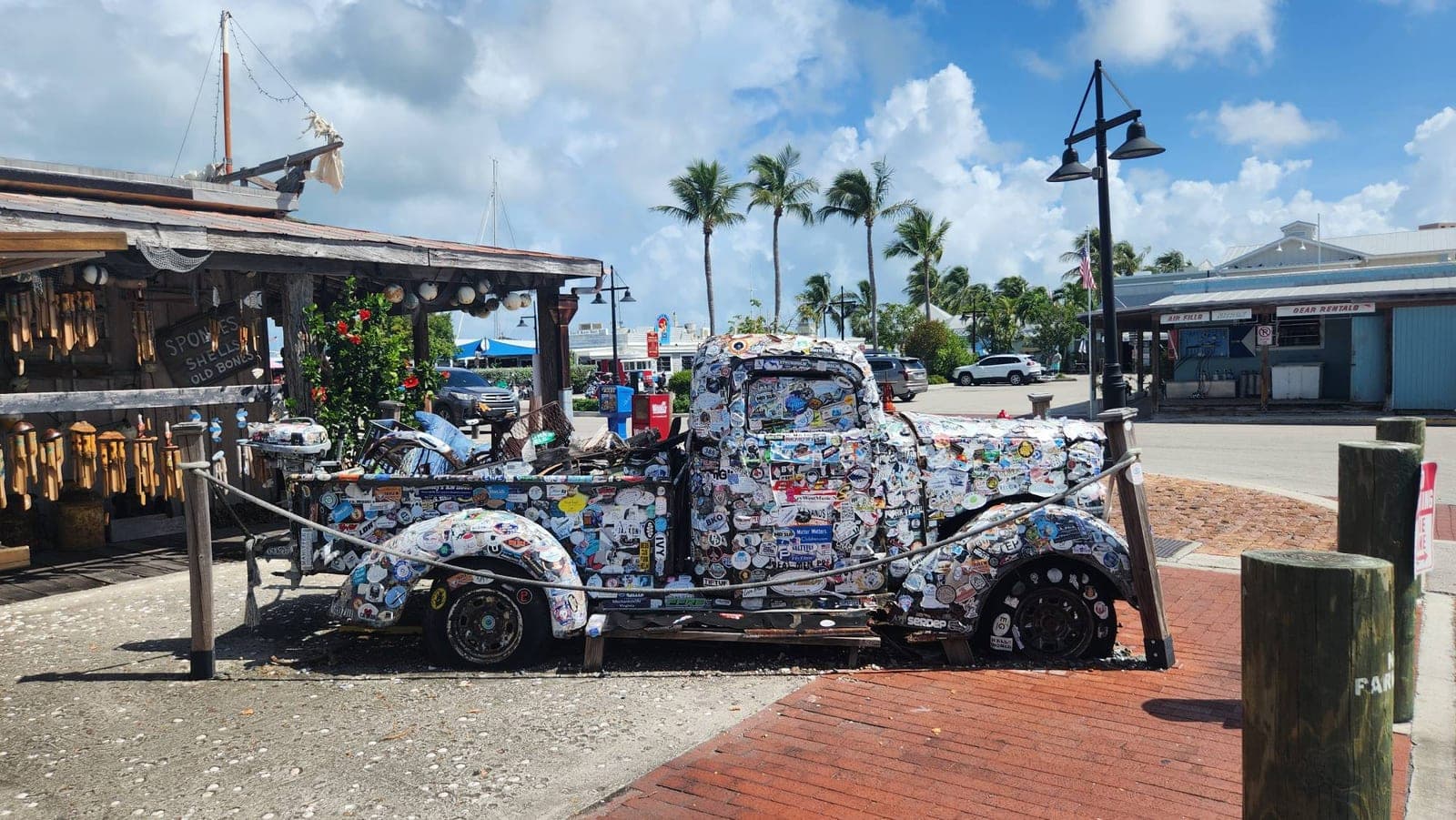 A vintage truck completely covered in bumper stickers, parked outside a shop near the Historic Seaport