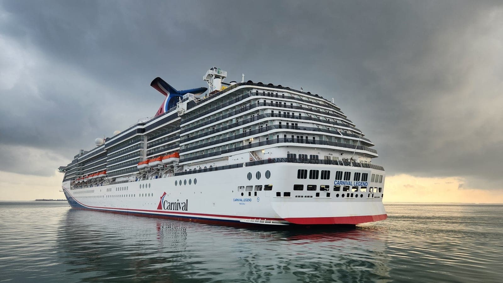 Carnival Legend underway at sea beneath a dramatic stormy sky at sunset