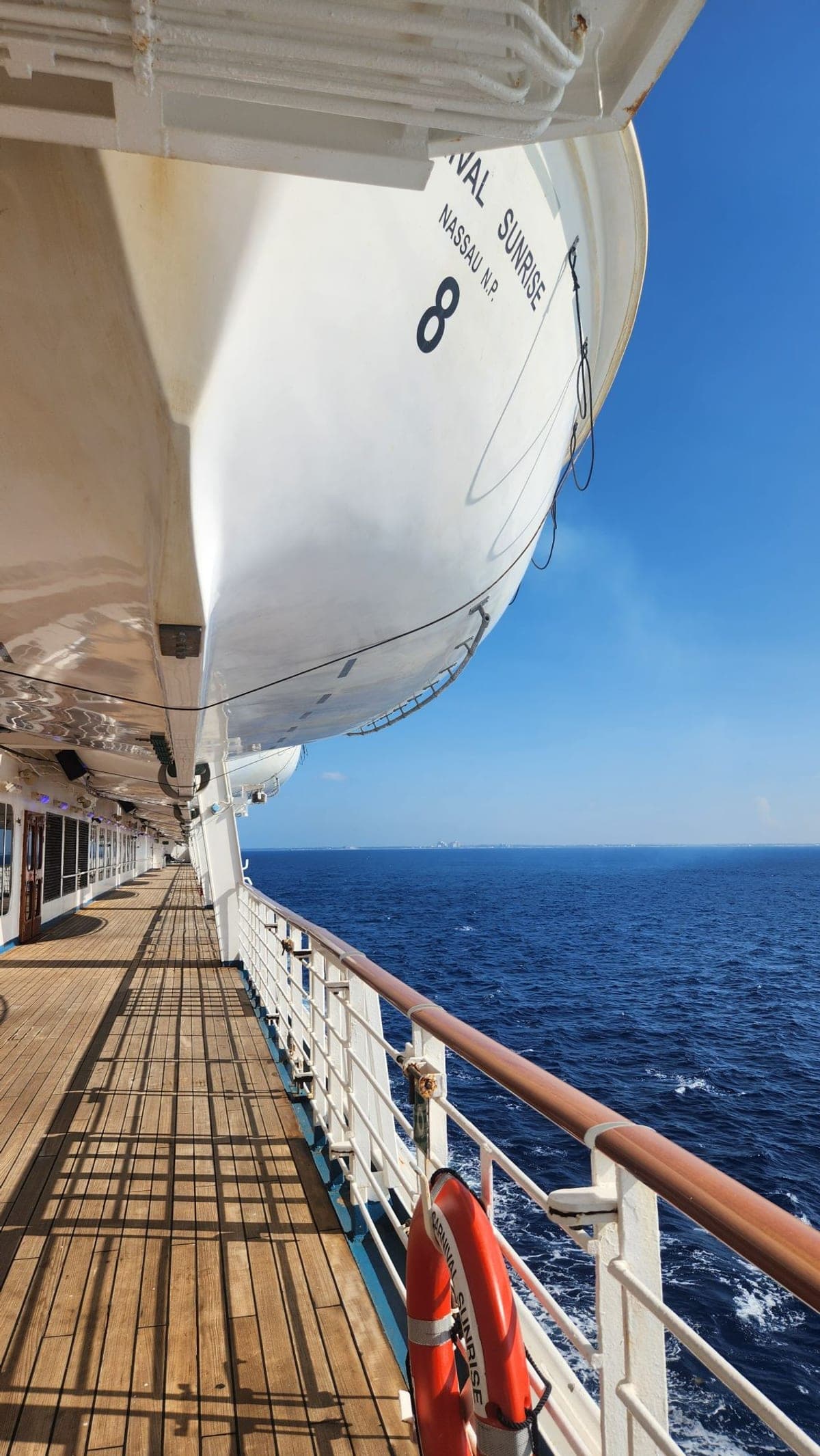 A lifeboat marked 'Carnival Sunrise Nassau N.P. 8' hanging over the ship's open promenade deck at sea
