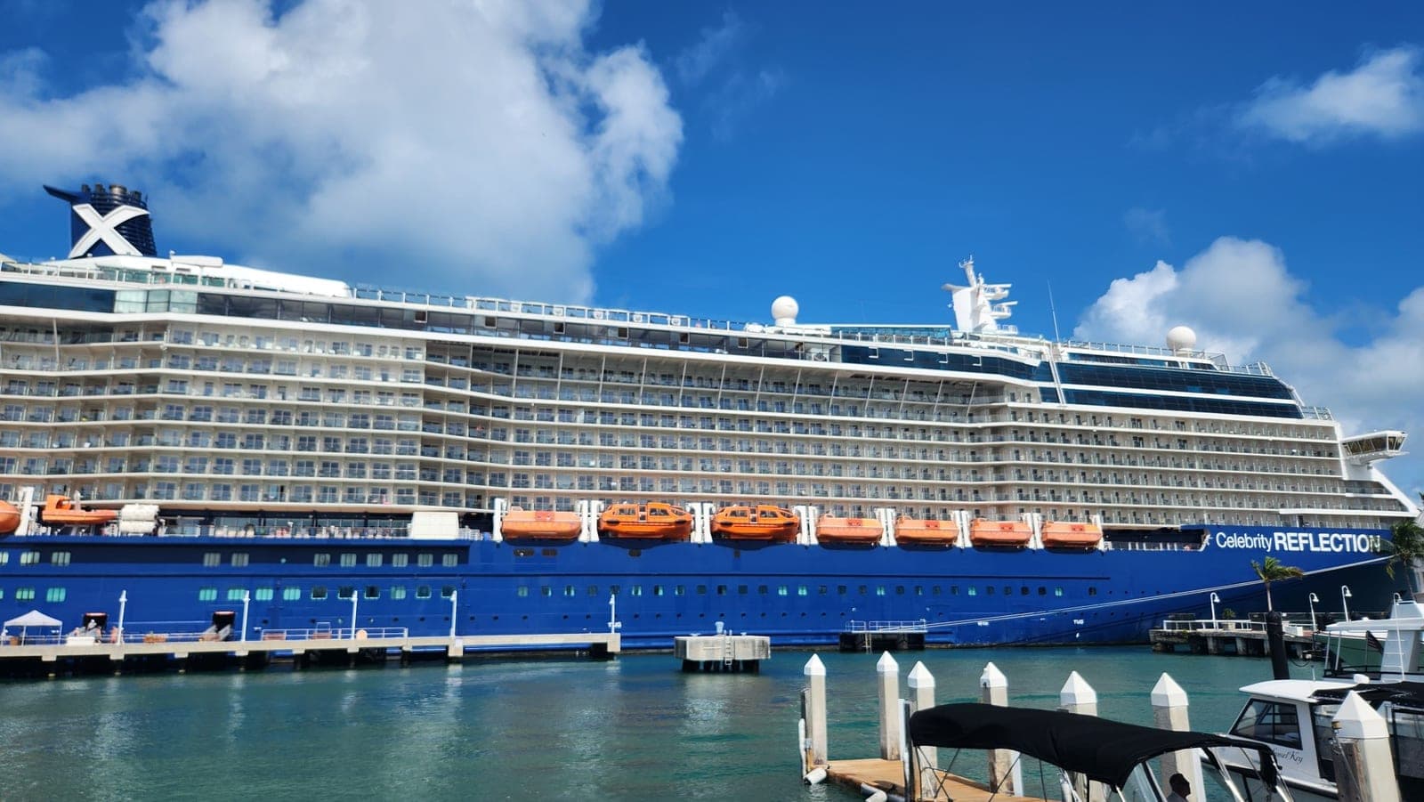 Celebrity Reflection docked, viewed from the pier with orange lifeboats and the ship's blue hull
