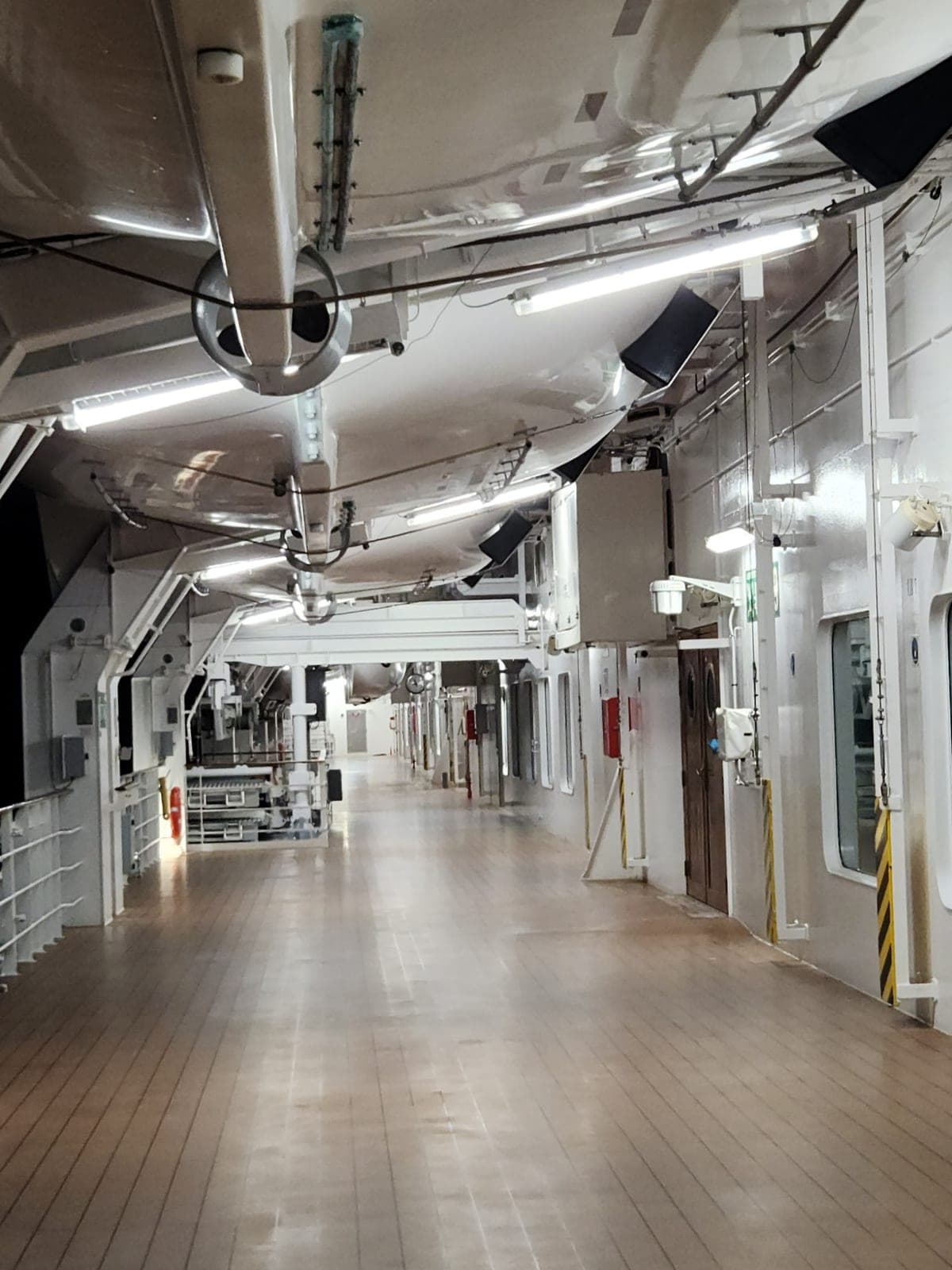 A working corridor aboard MSC Magnifica lined with lifeboats, pipework, and crew doorways