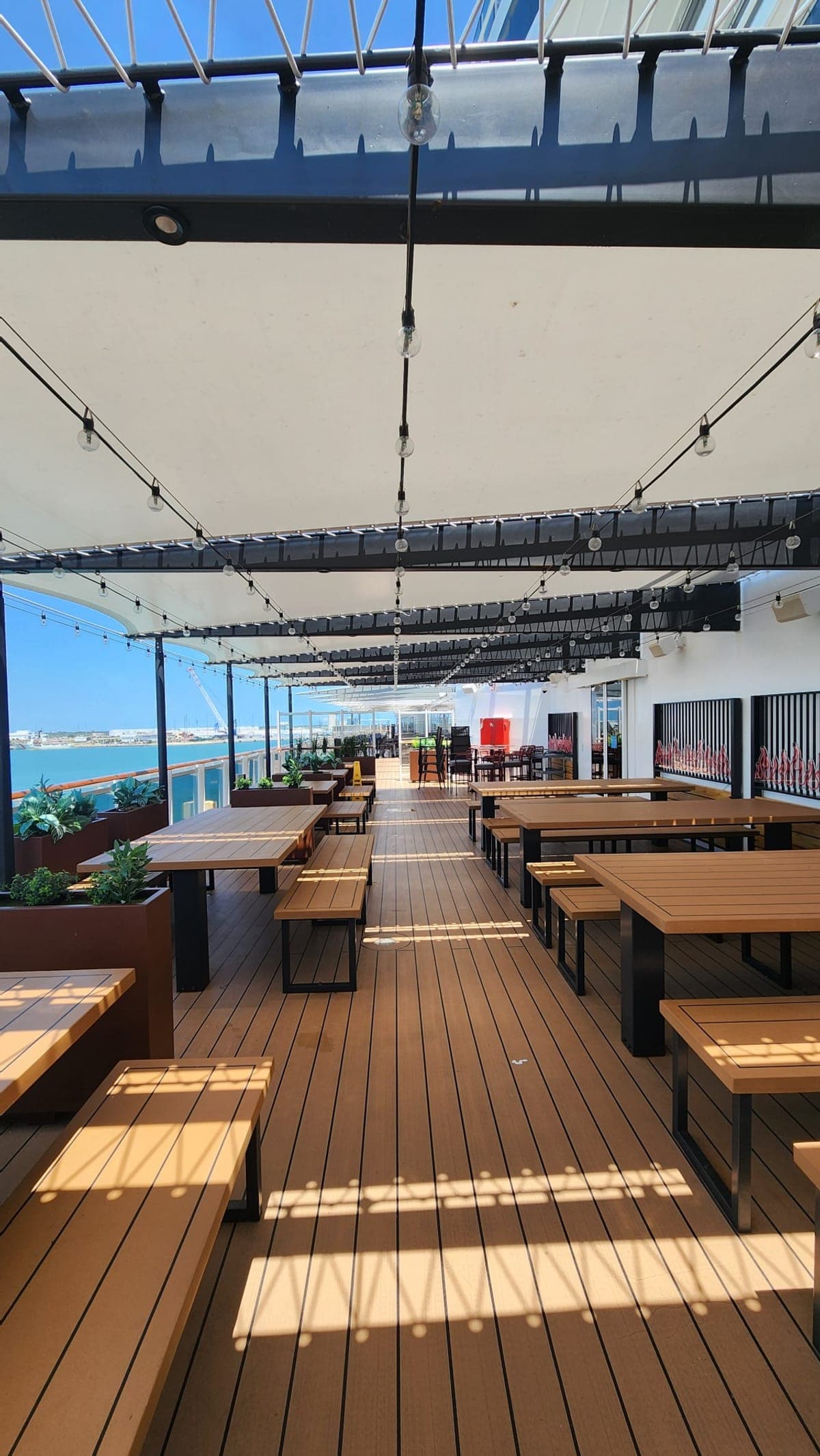A covered outdoor dining terrace aboard MSC Seashore with string lights, overlooking the port