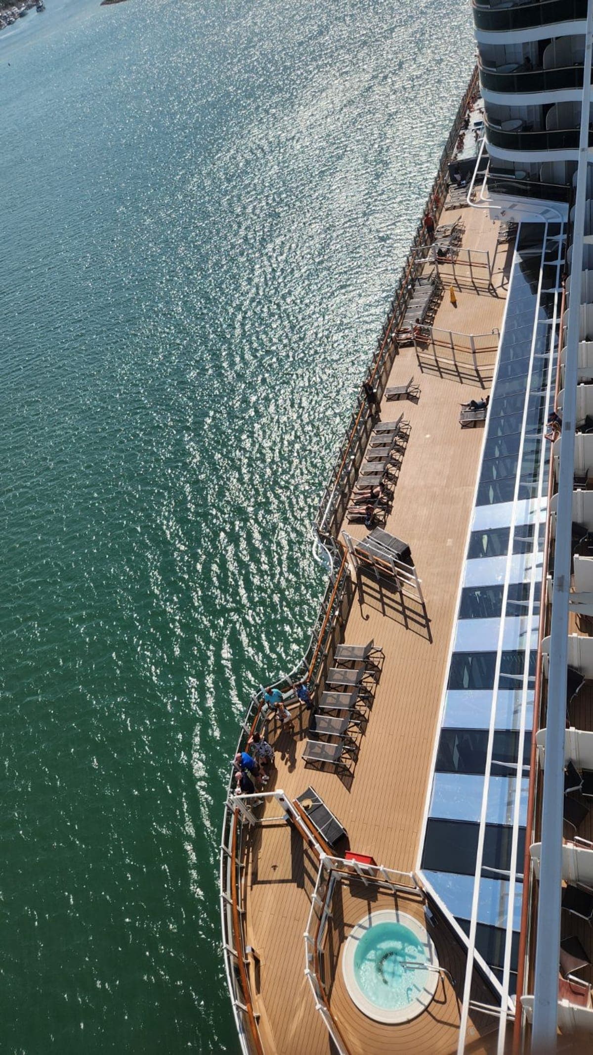 A curved side promenade deck aboard MSC Seashore lined with sunloungers and a single whirlpool