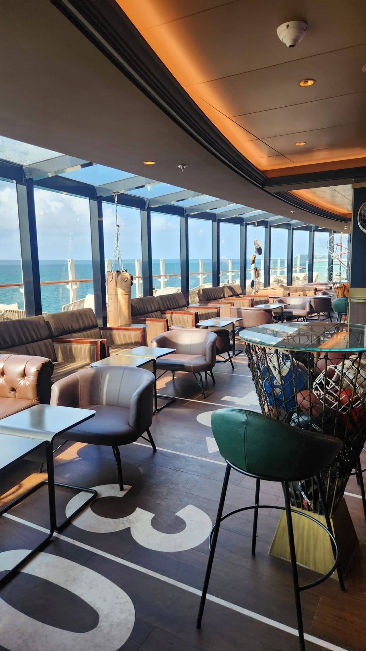 A sports-themed bar aboard MSC Seashore with yard-line floor markings, sports equipment, and ocean views