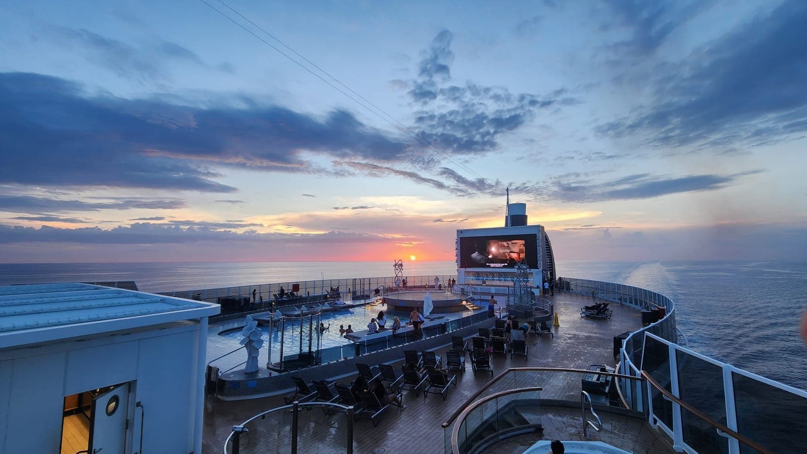 MSC Seashore's aft pool deck at sunset with the outdoor movie screen lit up over the water