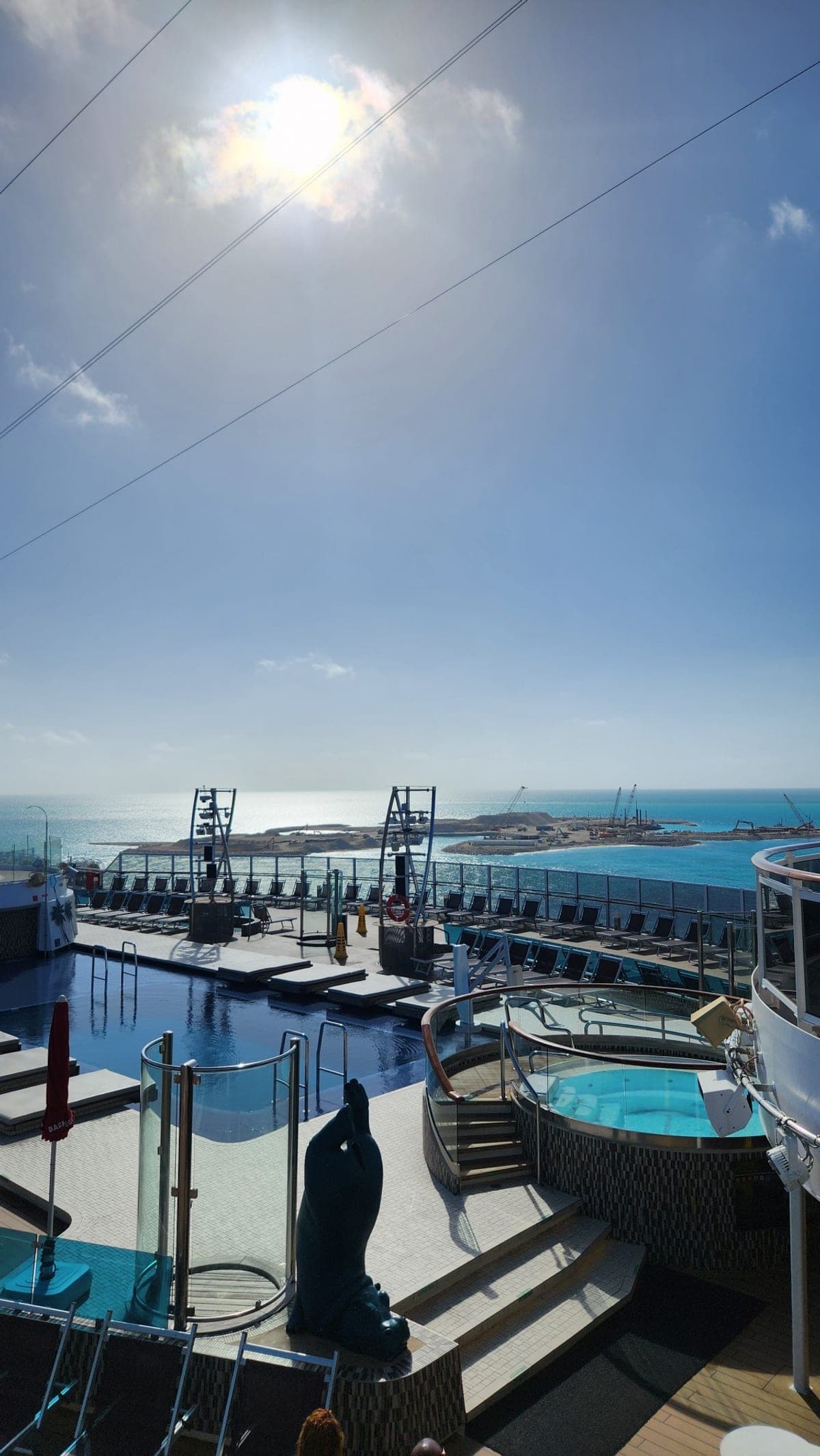 An upper-deck pool and hot tub aboard MSC Seaside overlooking Ocean Cay MSC Marine Reserve in the distance